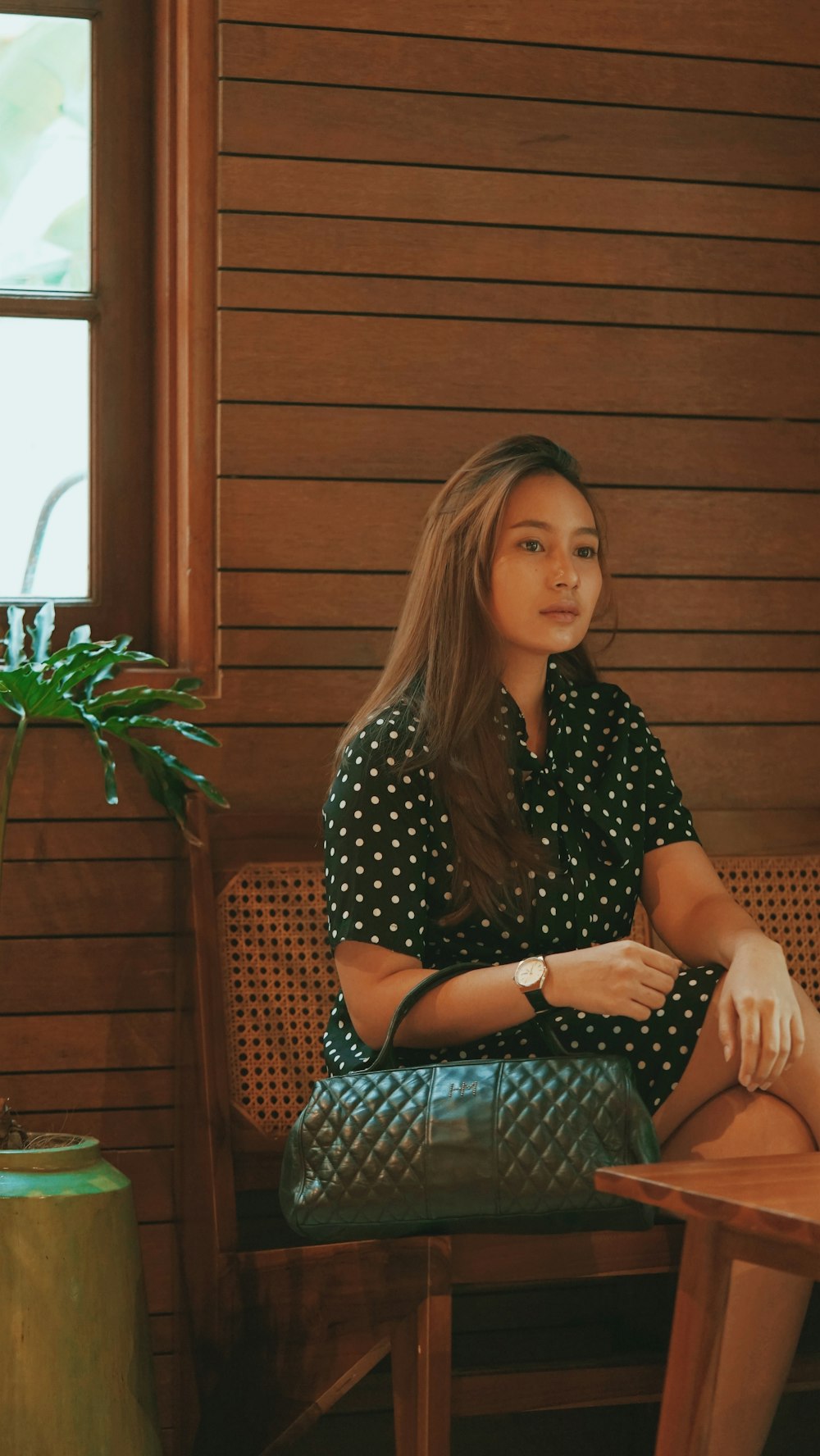 woman in black and white polka dot shirt sitting on brown wooden bench