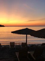 A scenic sunset over the calm sea at Cancún with silhouettes of beach loungers and umbrellas.