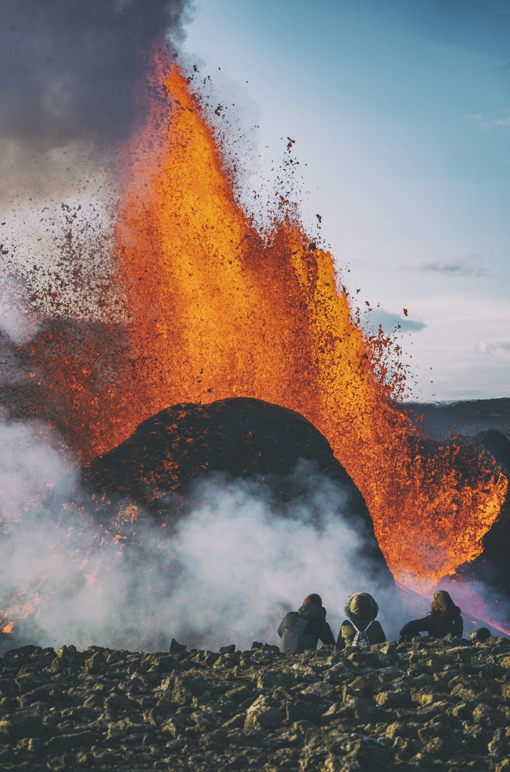 people standing on rock formation with fire during daytime