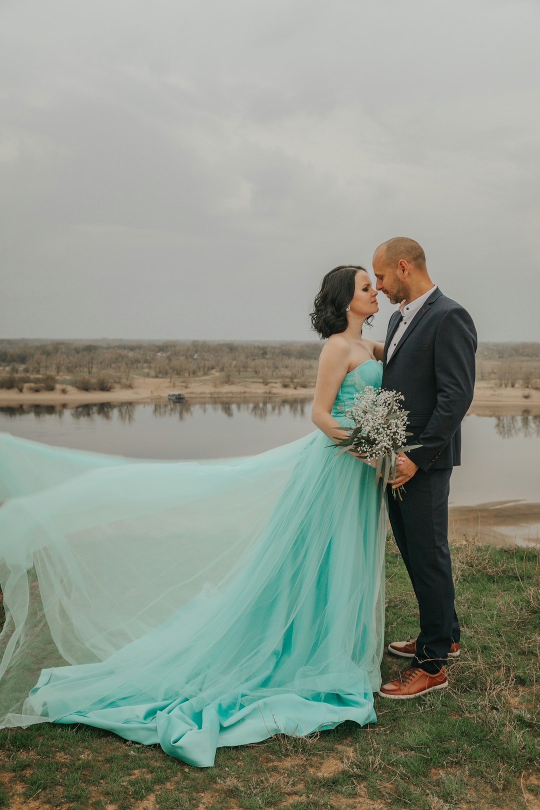 man in black suit and woman in teal dress holding bouquet of flowers