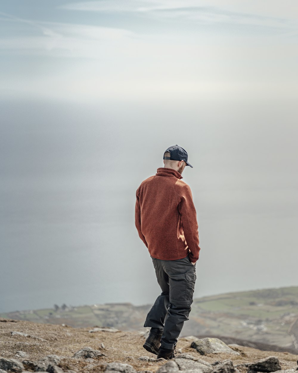 Hombre con chaqueta naranja y pantalones negros de pie sobre roca gris