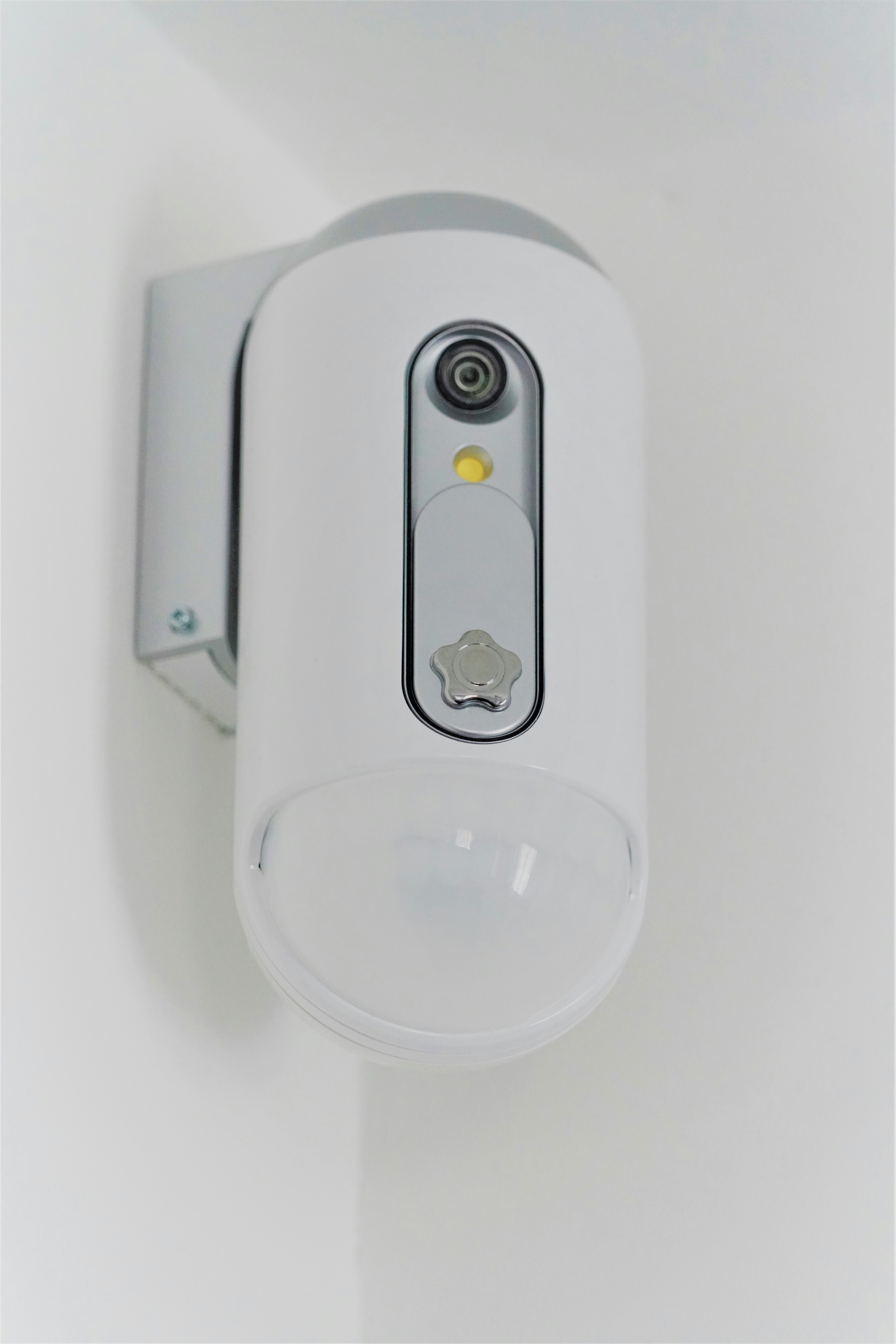 PIR motion detector sensor in white housing with mounting bracket, installed in corner of commercial room near ceiling