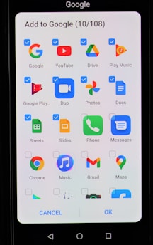 A smartphone screen displaying an interface to add applications to Google. The interface includes multiple app icons such as Google, YouTube, Drive, Play Music, Google Play, Duo, Photos, Docs, Sheets, Slides, Phone, Messages, Chrome, Music, Gmail, and Maps. Each app icon has a checkbox next to it, some of which are checked.