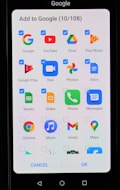 A smartphone screen displaying an interface to add applications to Google. The interface includes multiple app icons such as Google, YouTube, Drive, Play Music, Google Play, Duo, Photos, Docs, Sheets, Slides, Phone, Messages, Chrome, Music, Gmail, and Maps. Each app icon has a checkbox next to it, some of which are checked.
