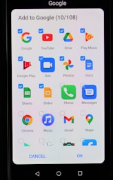 A smartphone screen displaying an interface to add applications to Google. The interface includes multiple app icons such as Google, YouTube, Drive, Play Music, Google Play, Duo, Photos, Docs, Sheets, Slides, Phone, Messages, Chrome, Music, Gmail, and Maps. Each app icon has a checkbox next to it, some of which are checked.