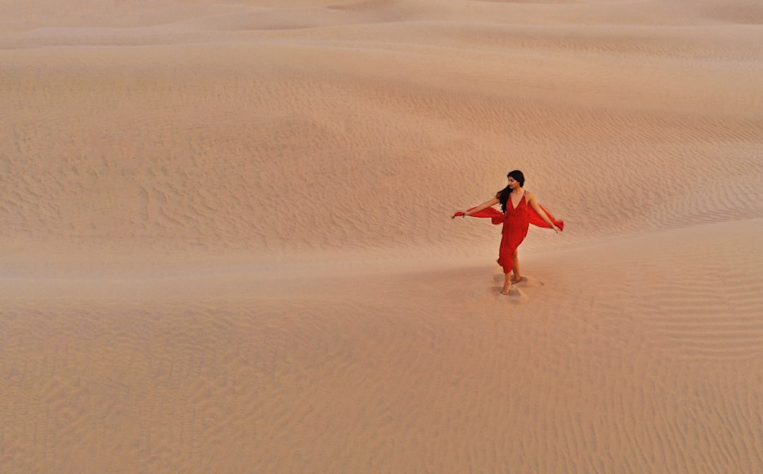 woman in red dress walking on brown sand