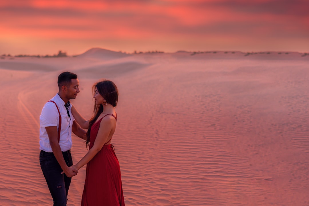 man and woman standing on seashore during sunset