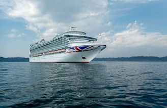 A vibrant red cruise ship cutting through calm blue waters under a sunny sky.