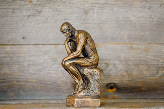 A bronze statue of a man in a pensive pose against a wooden background
