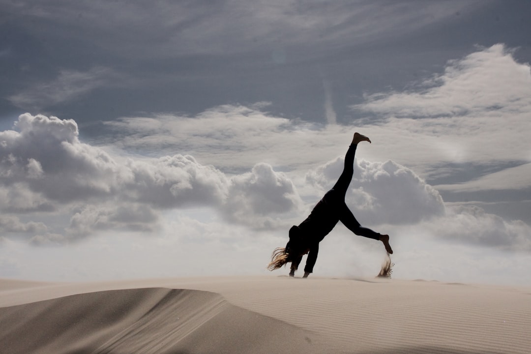 woman in black long sleeve shirt and black pants jumping on brown sand during daytime