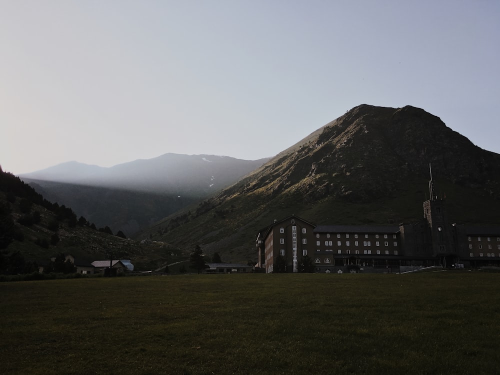 brown and white concrete building near green mountain under white sky during daytime