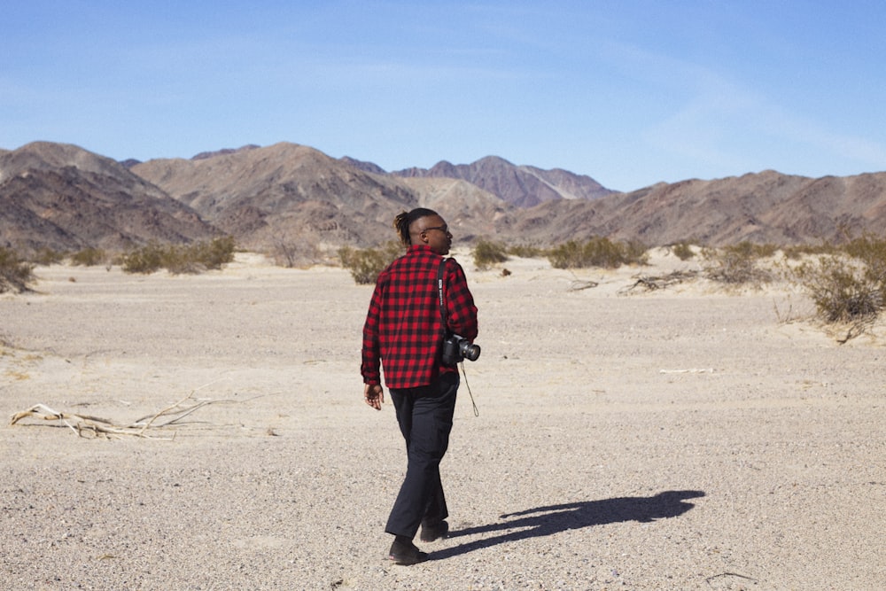 man in red and black plaid dress shirt and black pants walking on gray sand during