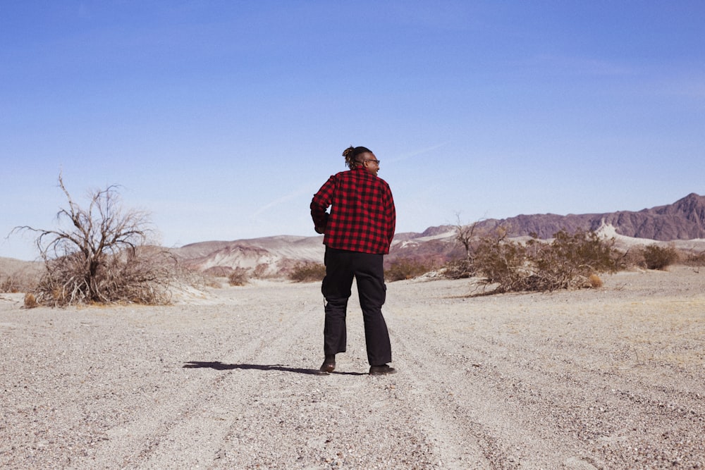 man in red and black plaid dress shirt and black pants walking on gray sand during