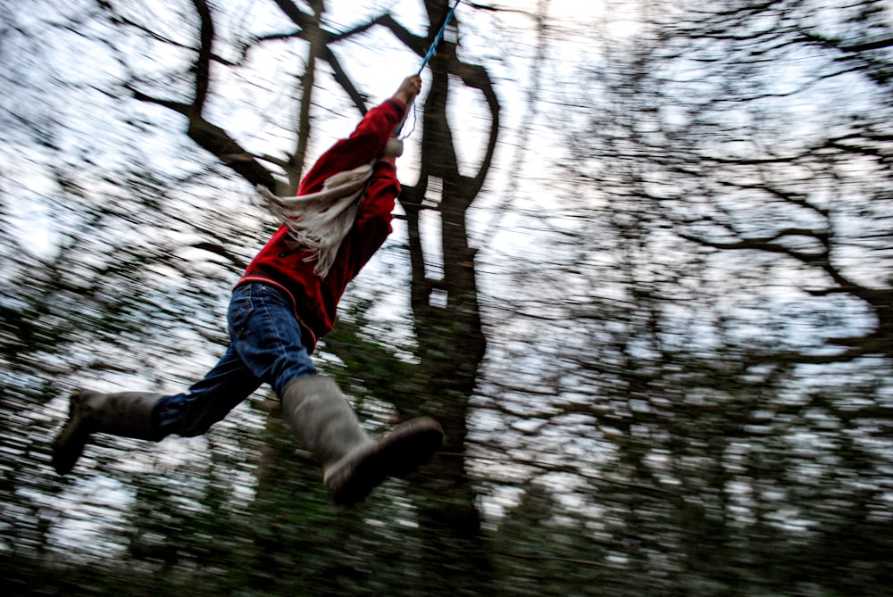 man in white shirt and blue denim jeans jumping on brown tree branch during daytime