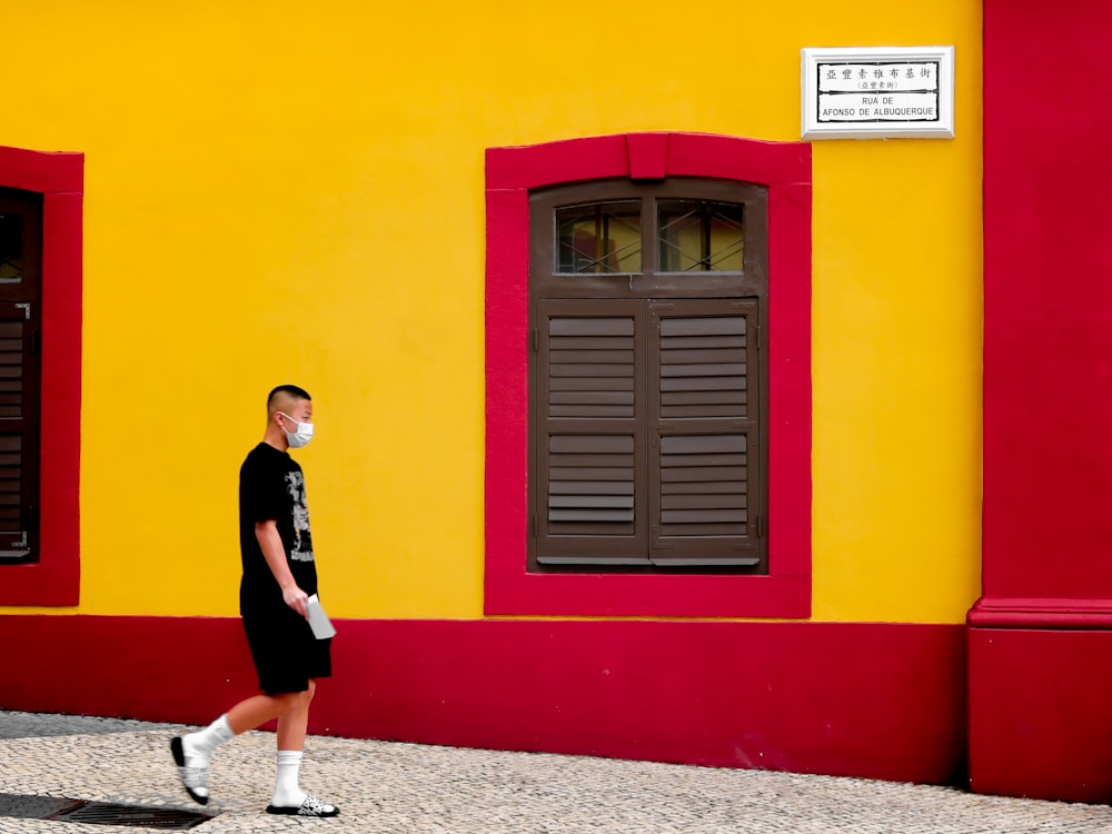 woman in black long sleeve shirt and red skirt standing beside yellow and red painted wall