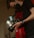 A person wearing a black mask is holding a professional camera with a label that reads 'BEN COLLINS BLACKMAGIC 1'. The person is wearing a black short-sleeved shirt and a blue wristband. The environment appears dimly lit, creating a focused and professional atmosphere.