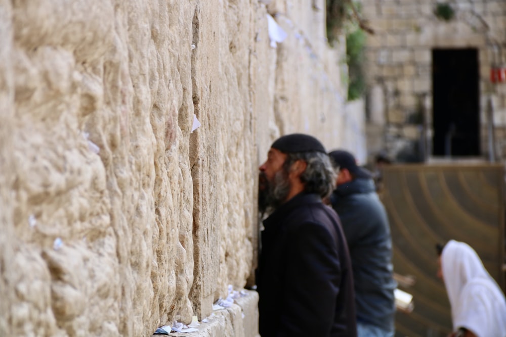 man in black jacket standing beside brown concrete wall during daytime