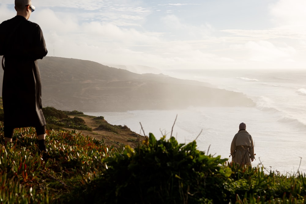 man in gray jacket standing on green grass near body of water during daytime