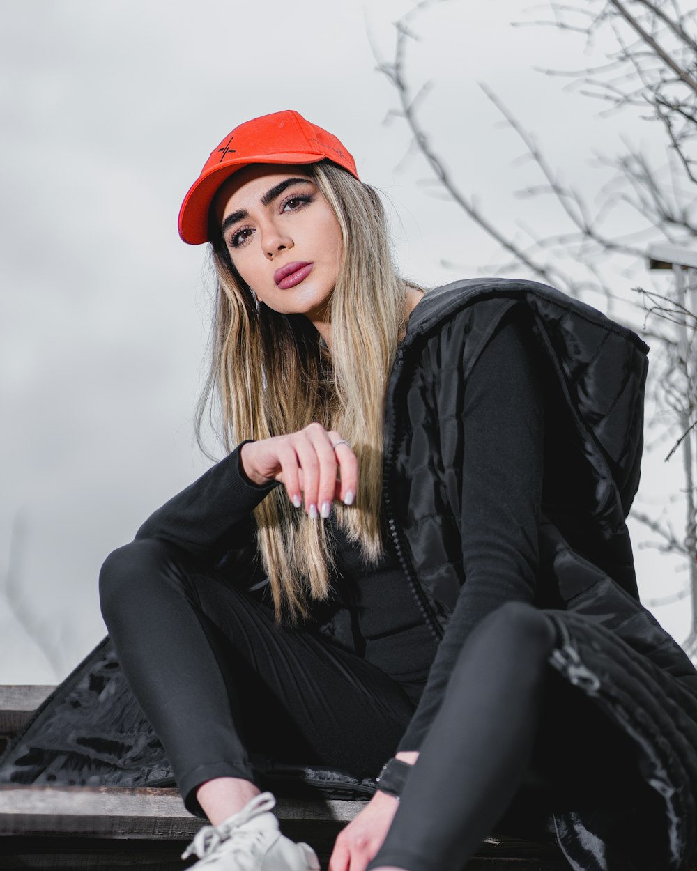 woman in black jacket and red knit cap sitting on rock