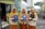 Three young women wearing matching mustard-colored hijabs and uniforms stand outside. Each holds a dark blue certificate folder embossed with a crest and a round medal in a red case. The background includes a building with green walls and an Indonesian flag.