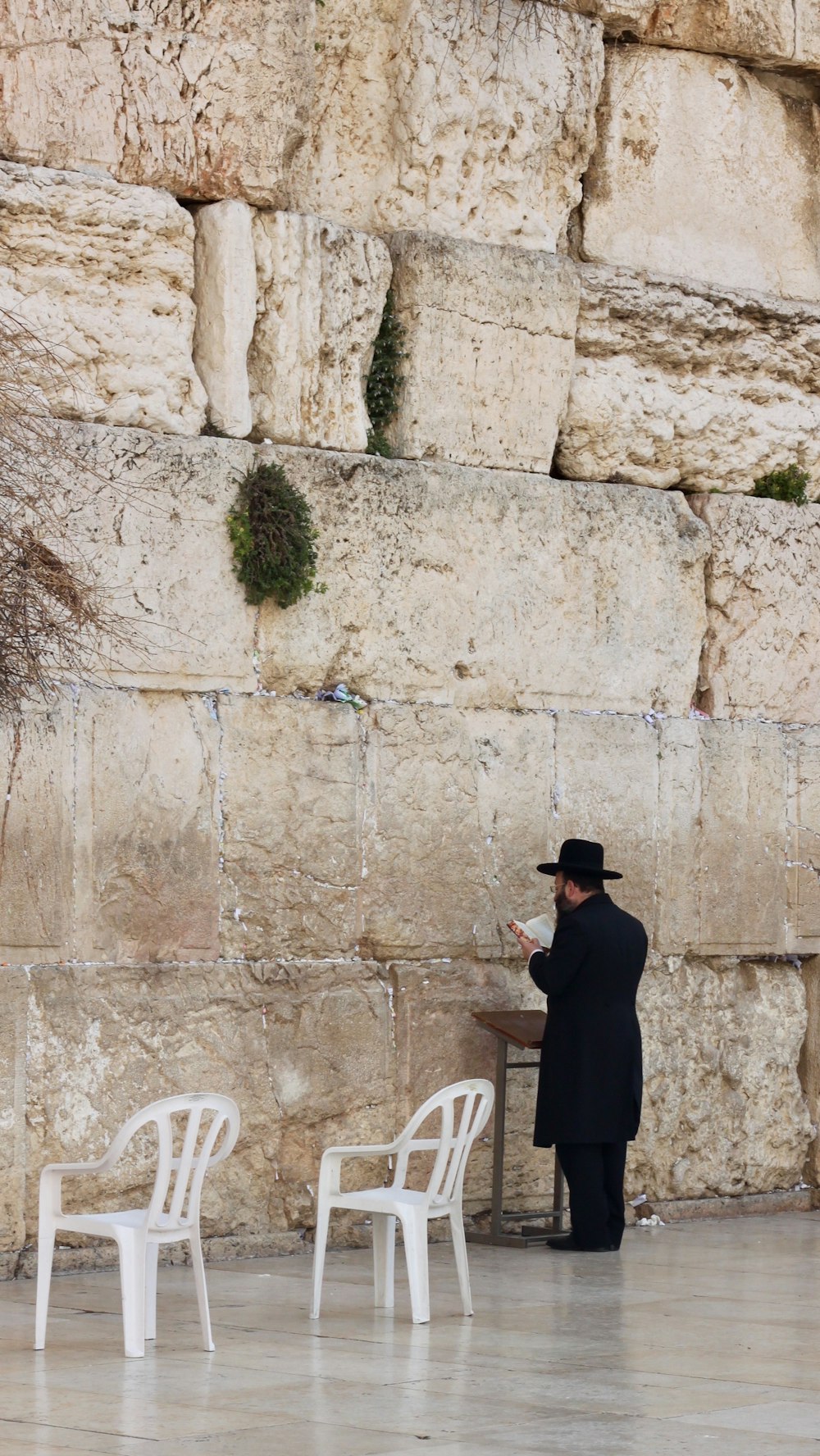 man in black suit standing beside white plastic chair during daytime