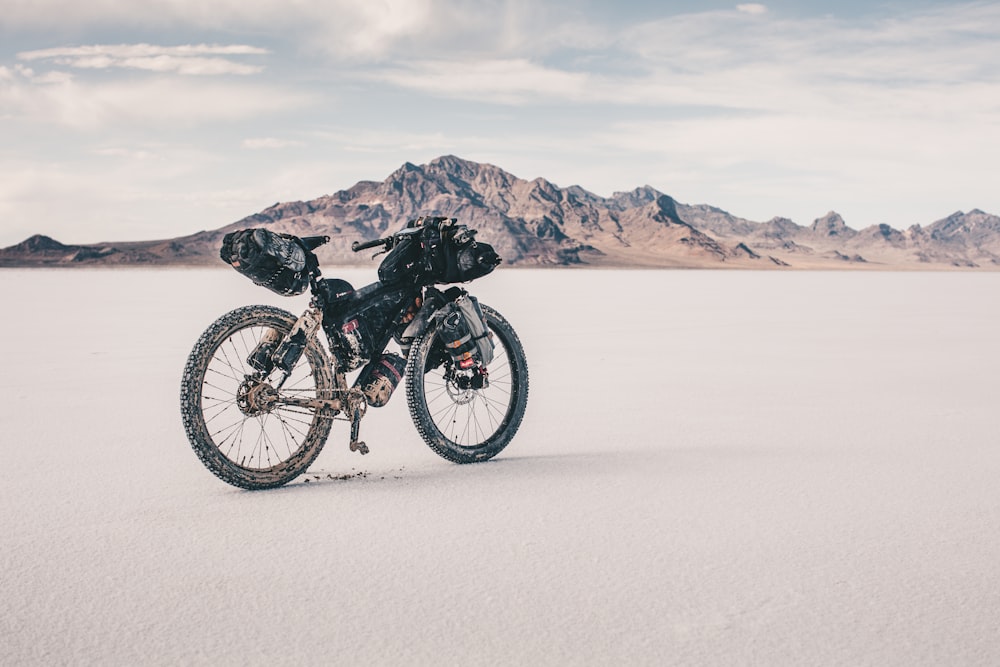 mountain bike preta na areia branca perto do corpo de água durante o dia