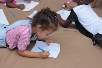 girl in pink and white stripe shirt writing on white paper