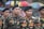 A group of men wearing military-style uniforms with camouflage patterns and black berets standing together in a formation. The uniforms have patches and name tags visible. In the background, there are colorful umbrellas.