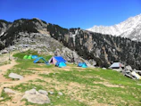blue and green tent on green grass field near gray rocky mountain during daytime