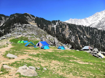 blue and green tent on green grass field near gray rocky mountain during daytime