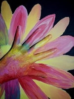 A hand covered in multicolored paint is laid on top of a large, vibrant painting of a flower. The petals of the flower are in shades of pink, yellow, and a touch of green against a dark background. The hand's paint colors blend harmoniously with the painted petals, creating an artistic and playful effect.