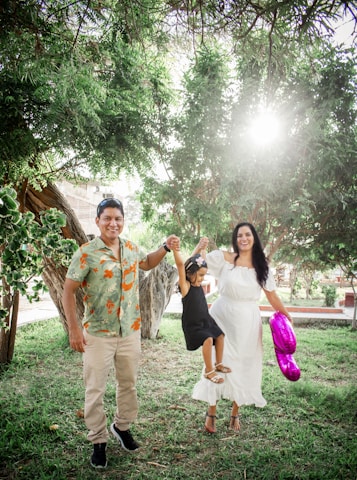 A smiling child with Down syndrome playing outdoors with family in a sunny park.