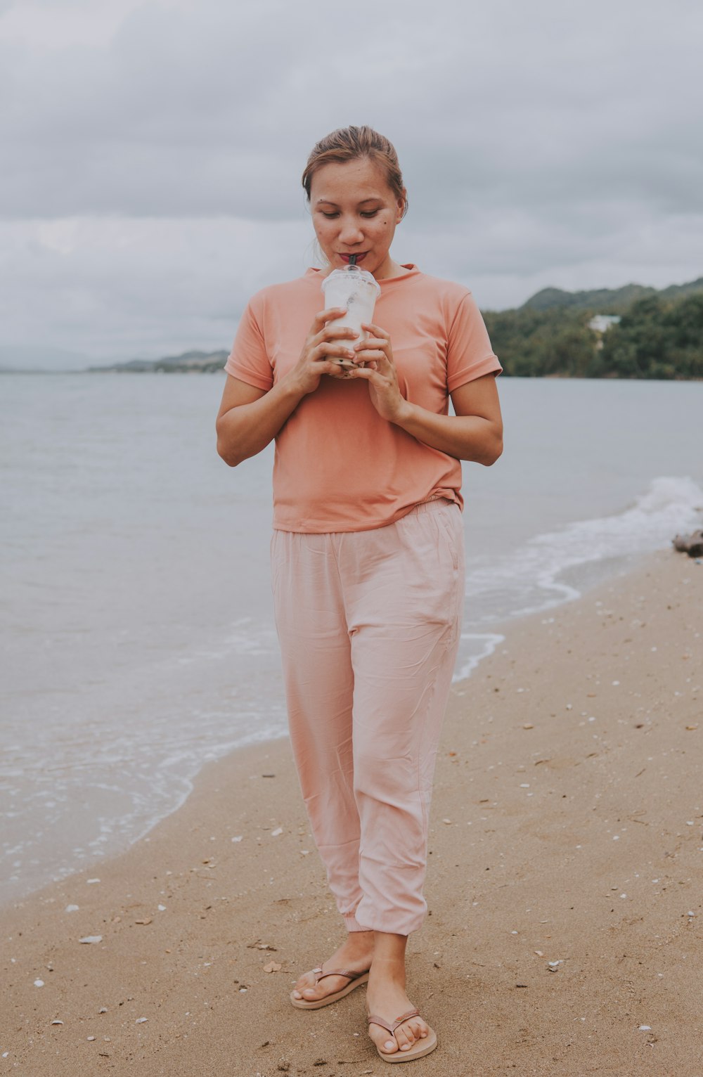 woman in pink tank top and white pants standing on beach shore during daytime