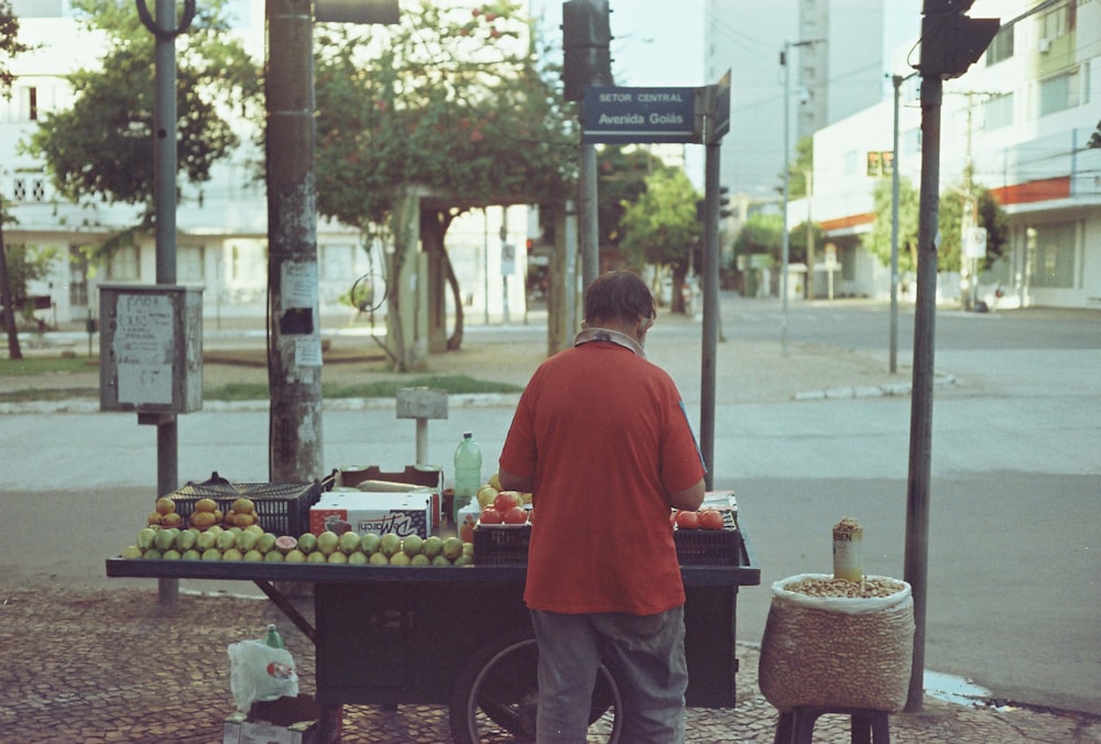 man in red shirt standing near fruit stand