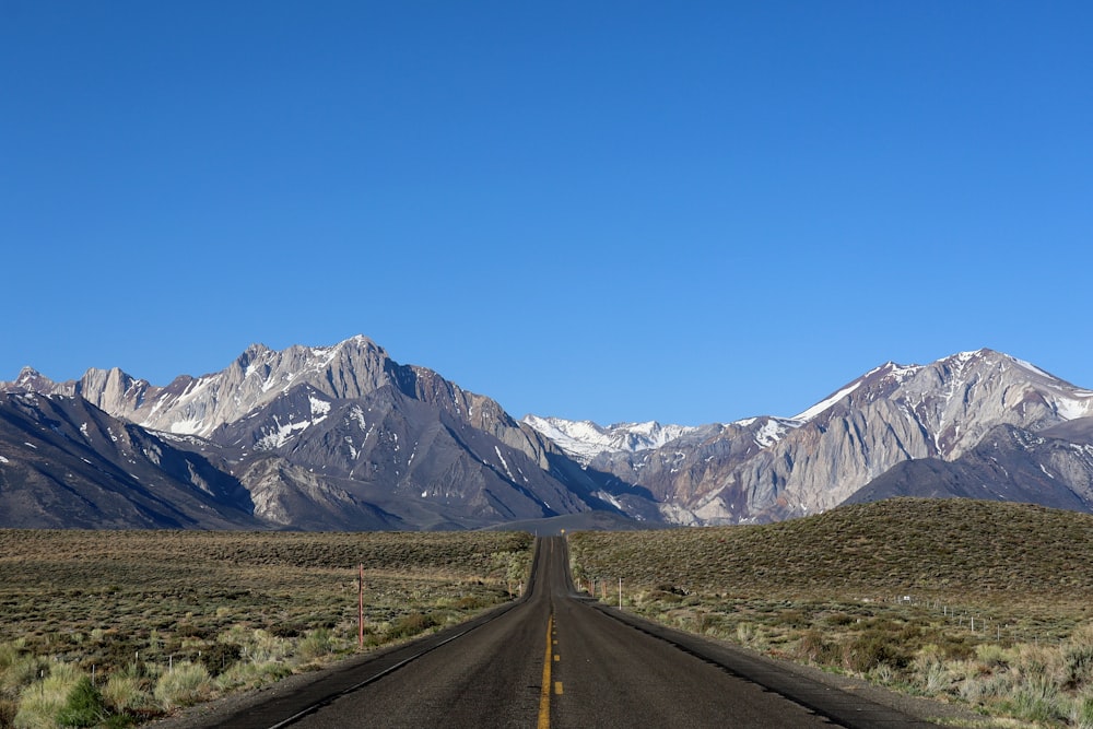 gray concrete road near mountain range under blue sky during daytime