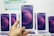 A hand is holding a boxed smartphone with a stylized purple and pink circle design on the front. Multiple identical smartphone boxes are displayed in the background.