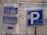 Street signs in Arabic and English are displayed on a wall with weathered surfaces. The largest sign shows a parking symbol 'P' with Arabic writing beneath it. Other signs provide information about the street, including historical references and street numbers.