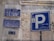 Street signs in Arabic and English are displayed on a wall with weathered surfaces. The largest sign shows a parking symbol 'P' with Arabic writing beneath it. Other signs provide information about the street, including historical references and street numbers.