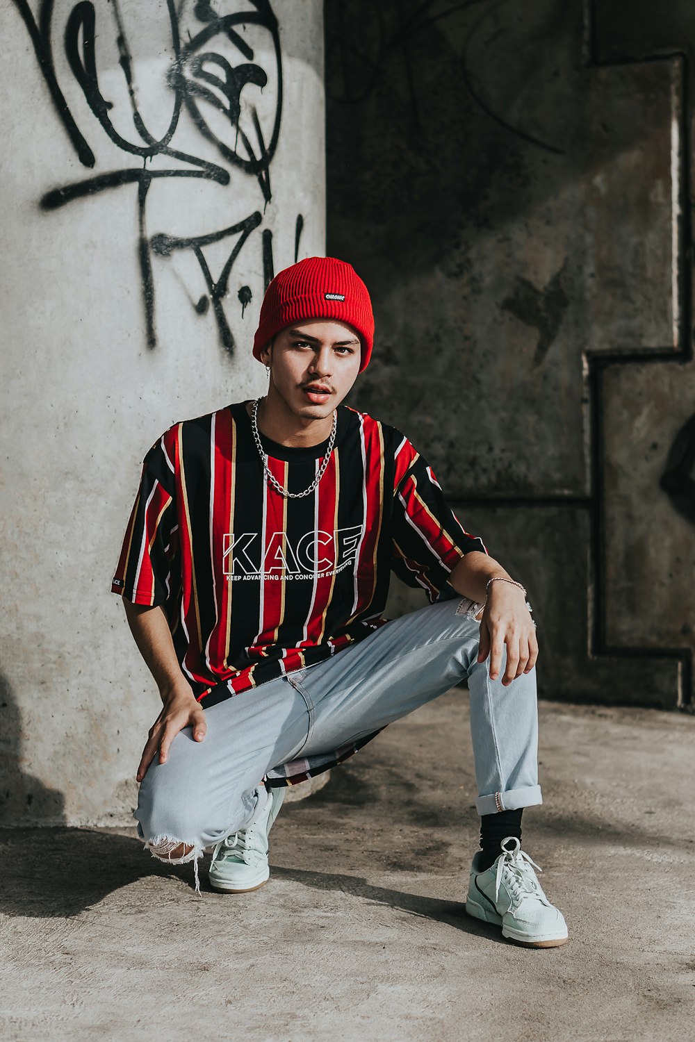 man in red and black stripe shirt and gray pants sitting on concrete wall during daytime