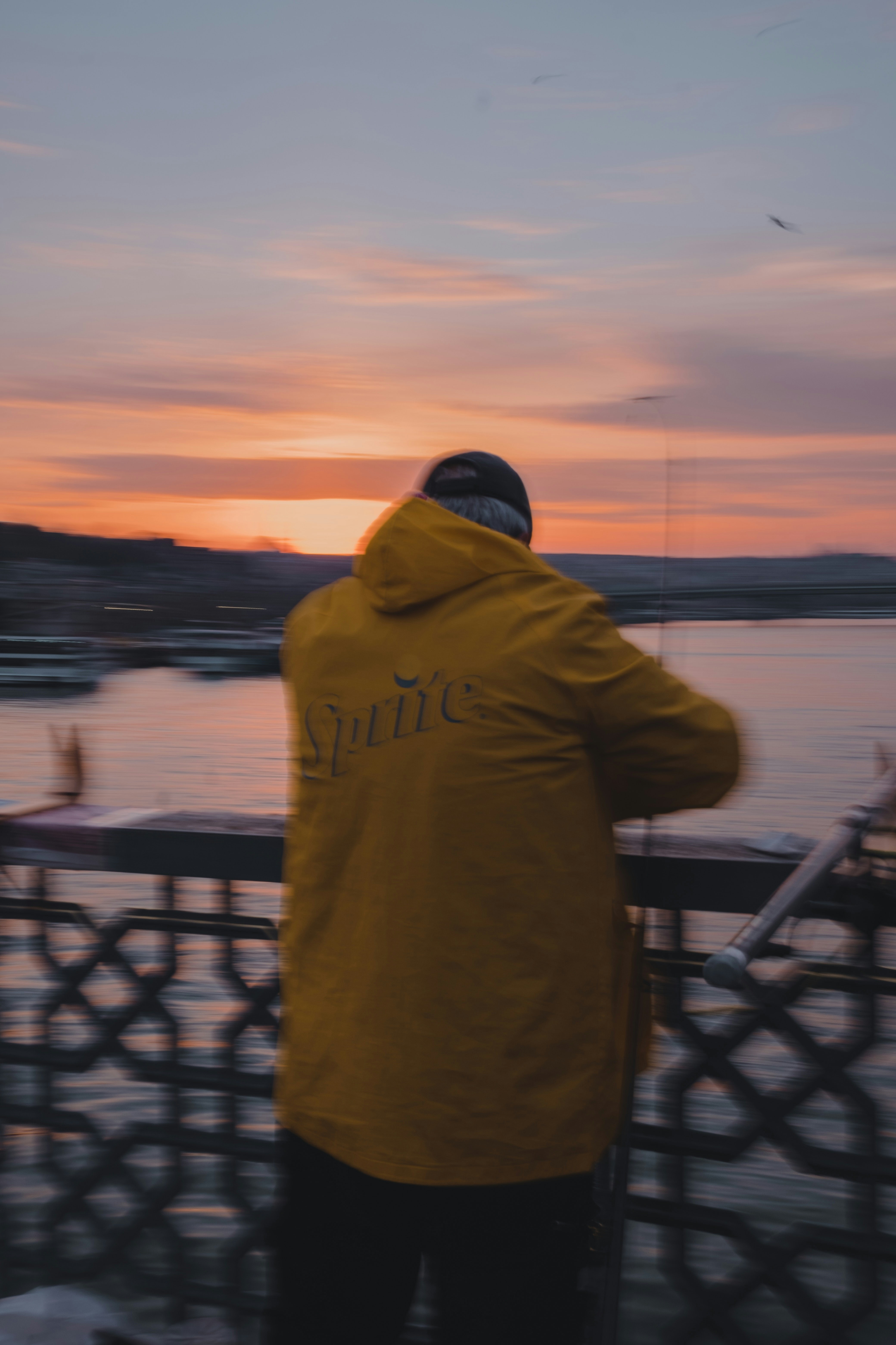 man in yellow hoodie standing near black metal railings during daytime
