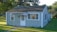 A small, single-story house with gray siding and a dark shingled roof. It features a white door with multiple panes of glass and has striped awnings over the front windows. The house is surrounded by a neatly trimmed lawn and several mature trees are visible in the background.