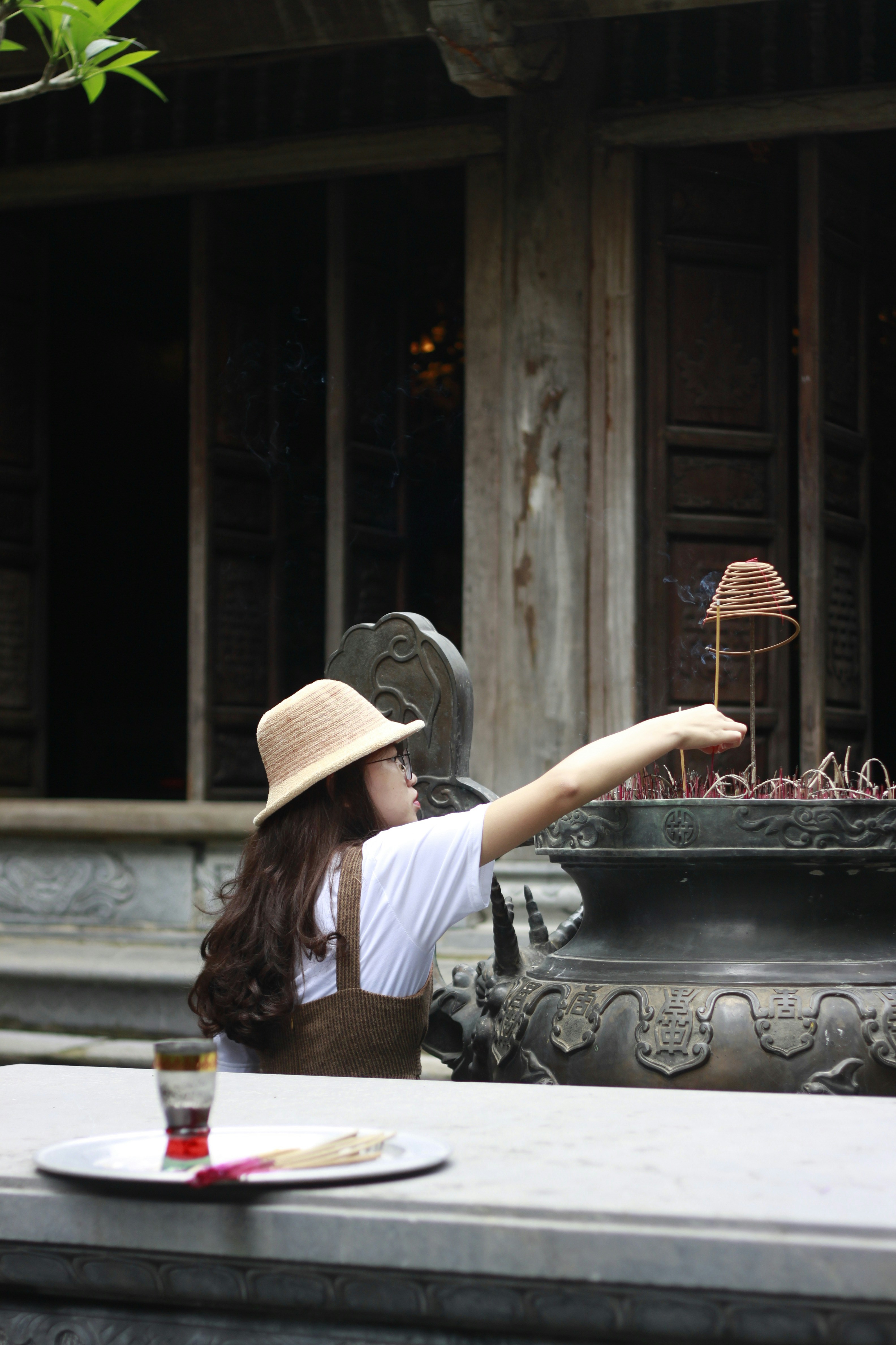 Femme en chemise blanche et chapeau marron debout devant une fontaine extérieure ronde en acier noir