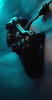 A video game controller with various buttons and a connected cable is seen positioned against a textured surface, illuminated by moody blue and teal lighting that casts a shadow.