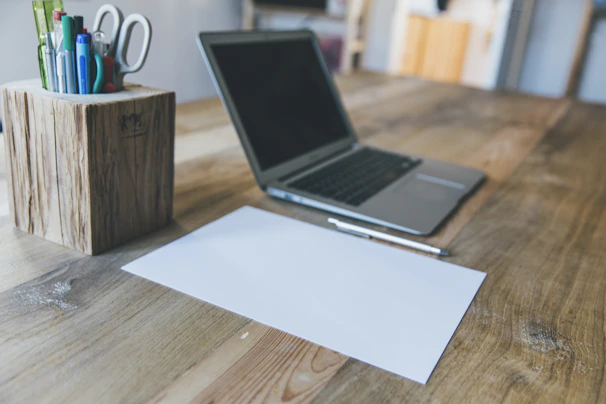 A person confidently writing a formal complaint letter at a wooden desk with a laptop and documents nearby.