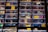A display of various sunglasses neatly arranged in rows. Each pair reflects a vibrant outdoor scene, likely with trees and a bright sky. The sunglasses vary in shape, size, and lens color, and some have price tags attached.