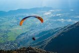person in black shirt with yellow parachute over the mountains during daytime