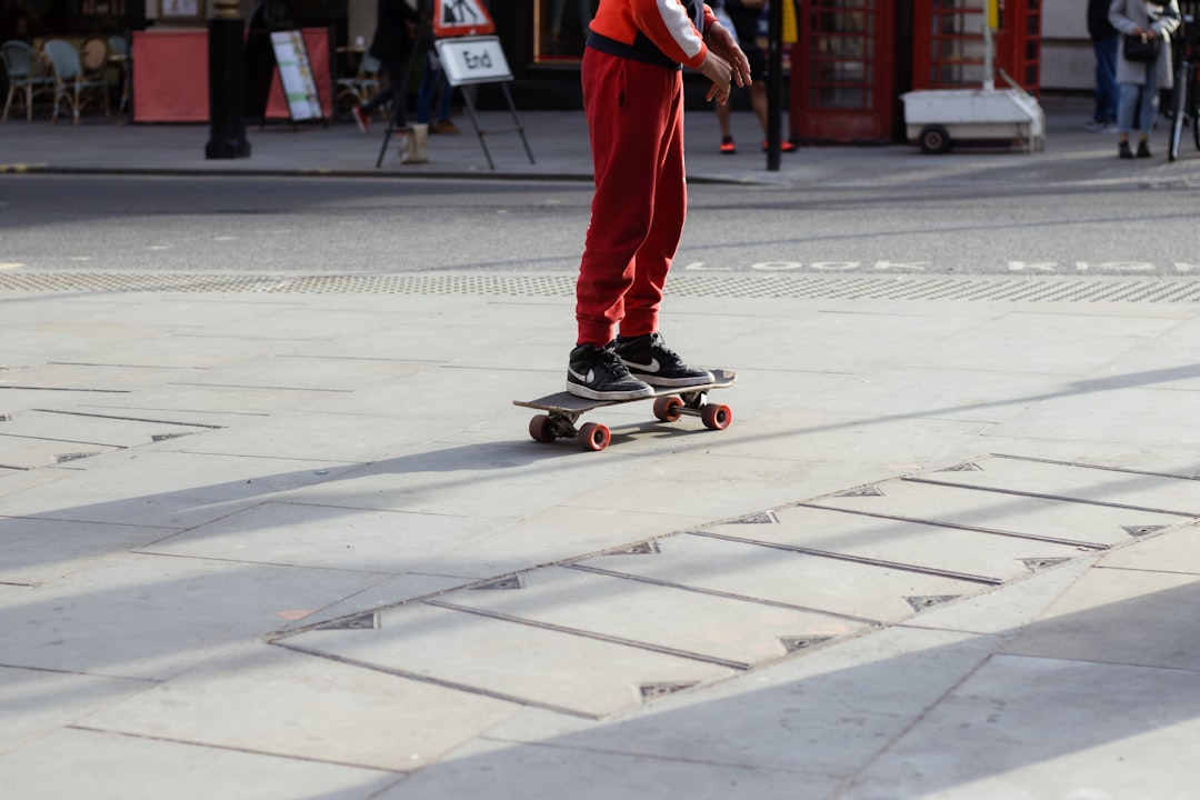 man in red pants and black shoes riding skateboard on gray concrete road during daytime