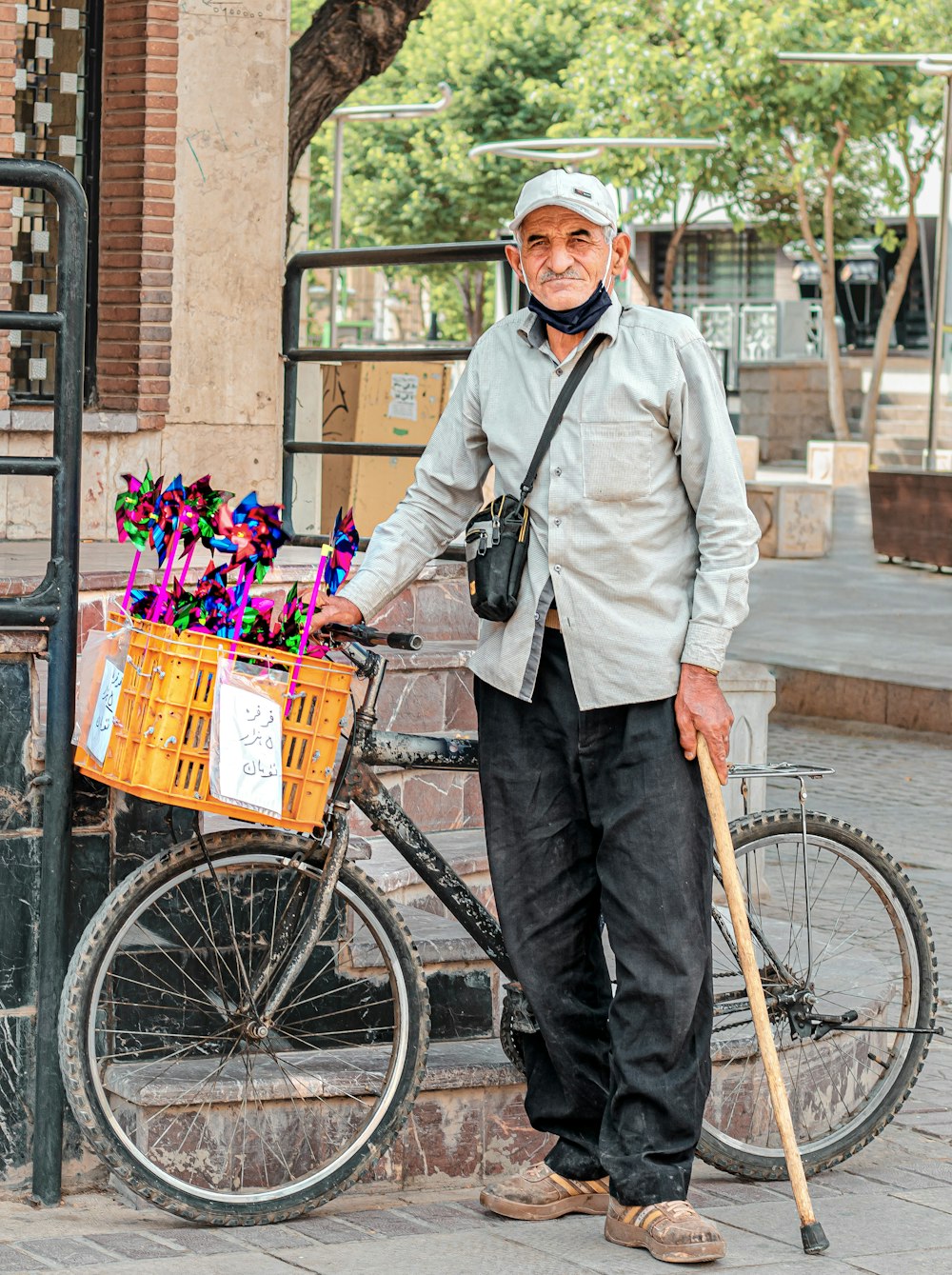 man in white dress shirt and black vest holding bicycle with basket of flowers