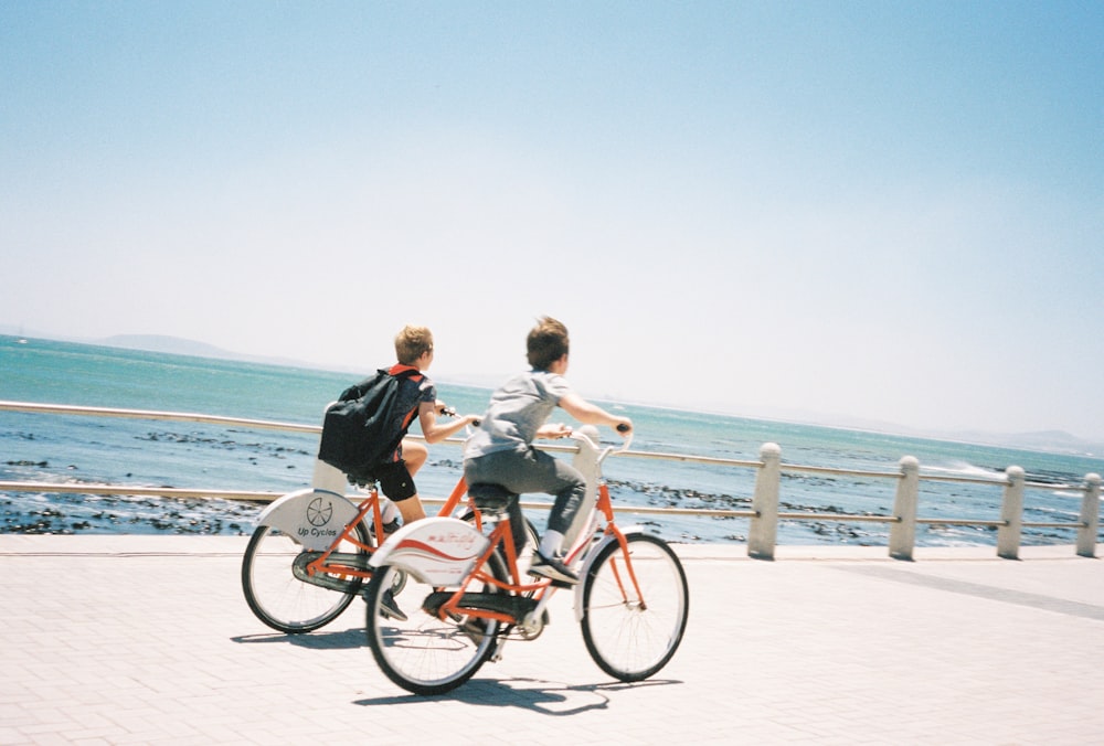 2 women riding on red bicycle on white sand beach during daytime