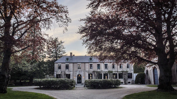 A serene, elegant estate home with a subtle sign of luxury estate sale discreetly placed on the gate.